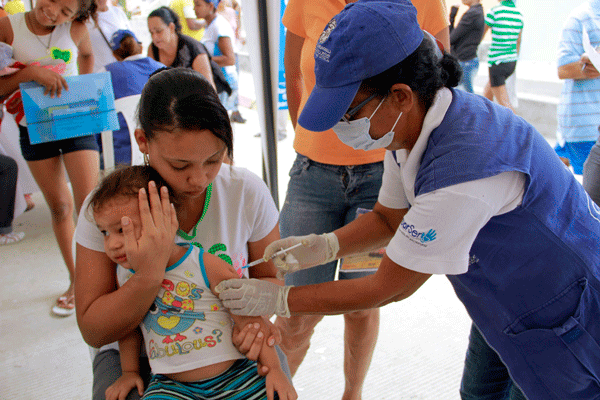 Funcionaria aplicando vacuna a niño en el brazo.