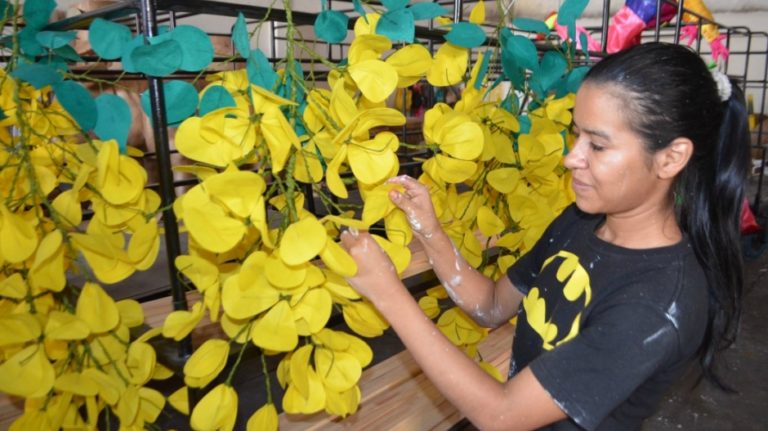 Joven, artista plástica exhibe creación de flores amarillas para carrosas.