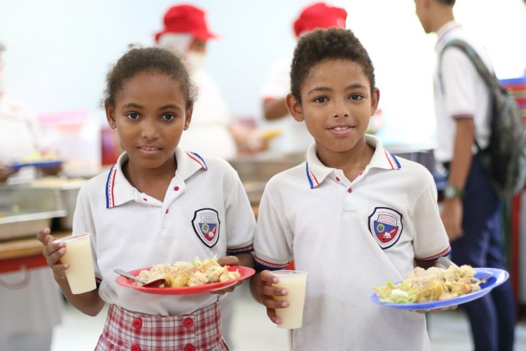 Niños uniformados con platos de alimentos en las manos