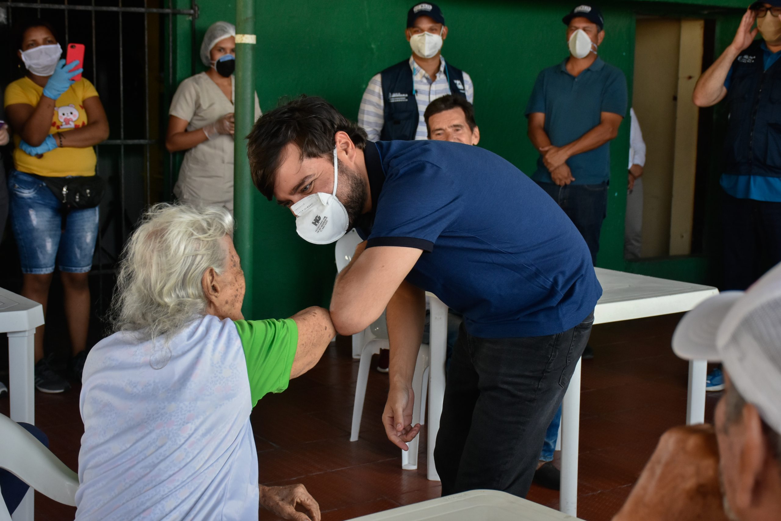 Alcalde saludando de codo a adulta mayor