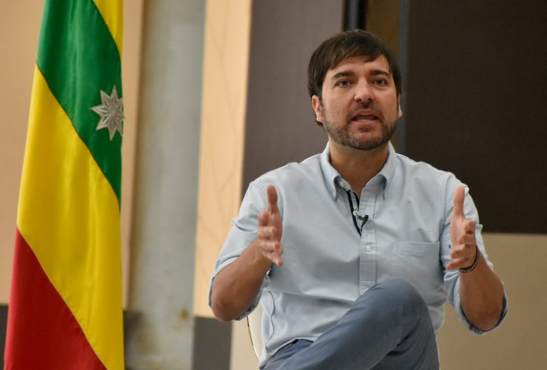 Alcalde sentado al lado de la bandera de Barranquilla