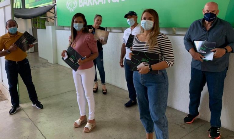 Varias personas usando mascarillas paradas frente a un letrero verde