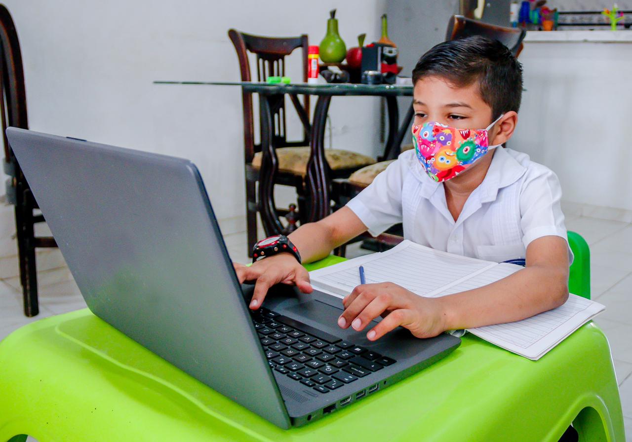 Niño con mascarilla escribiendo en laptop