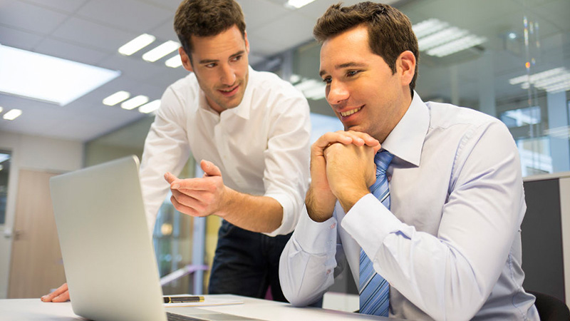 Dos hombres dialogando frente a un computador.