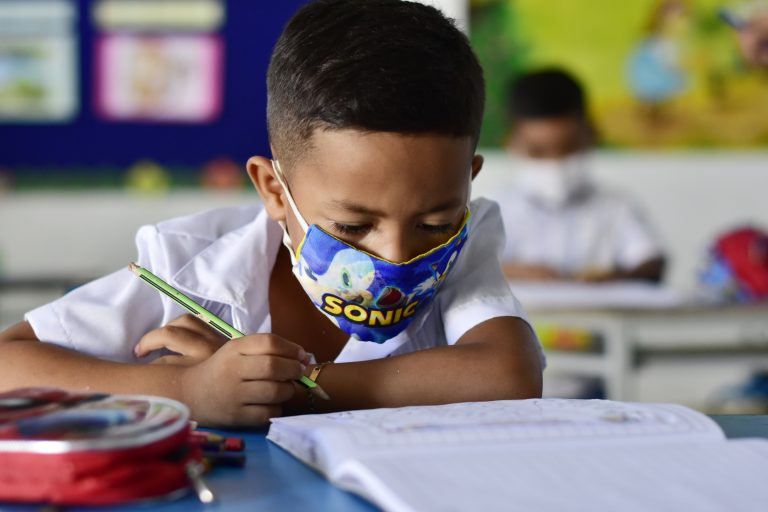 Niño escribiendo en salón de clases.