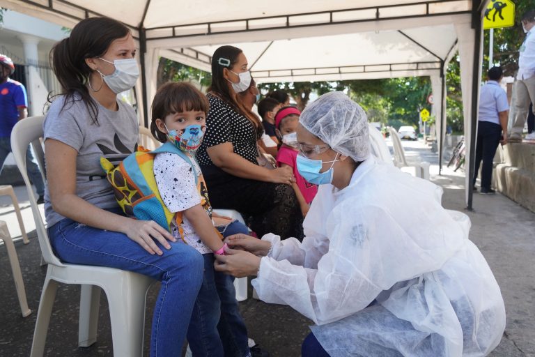 Funcionaria de la Secretaría de Salud, colocando manilla a niño.