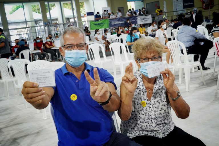 Pareja de ciudadanos mostrando certificado de vacunación con v en sus manos.