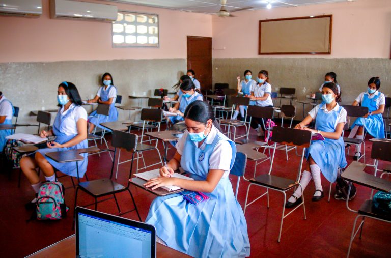 Mujeres Jóvenes en sus pupitres en salón de clases.