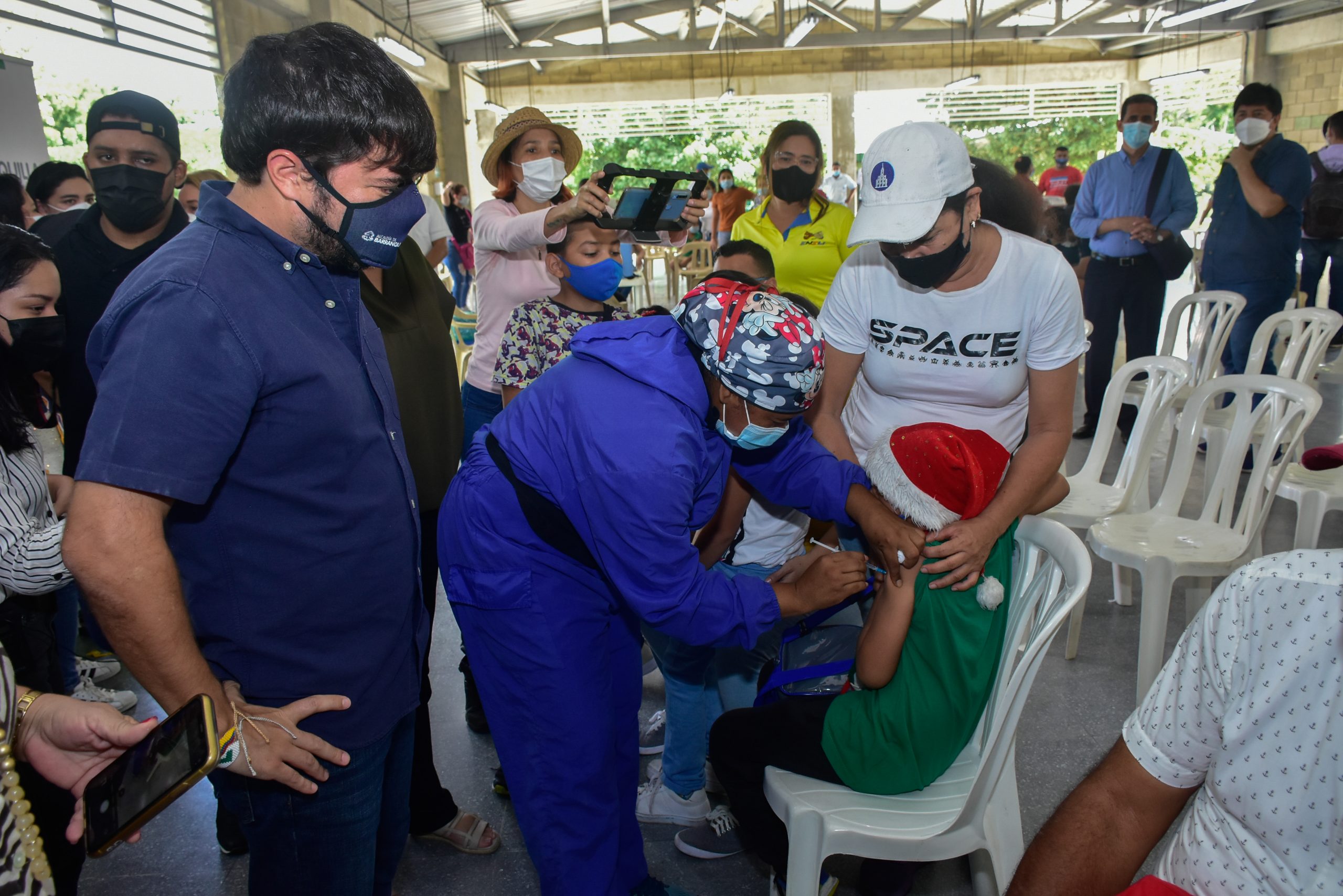 Alcalde Pumarejo observa a funcionaria que vacuna a niño.