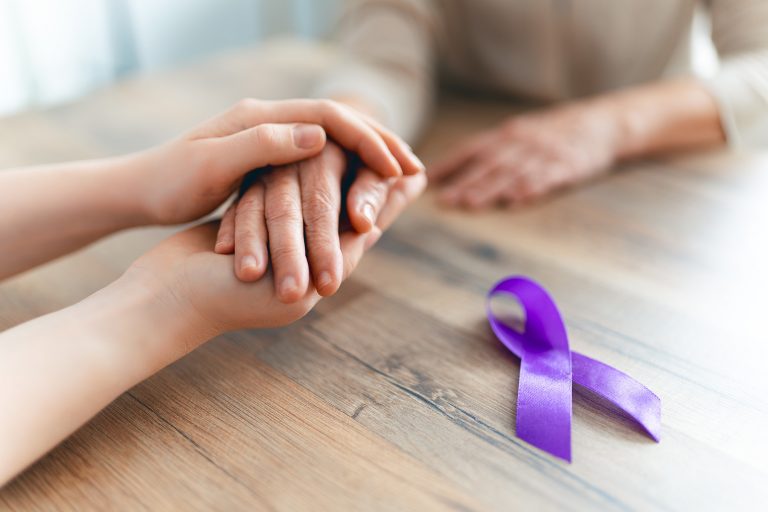 manos de dos personas entrelazadas y acompañadas de cinta de sìmbolo contra el cancer