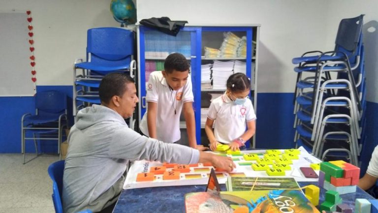 Docente en salon de robotica en compañia de dos estudiantes revisando un proyecto