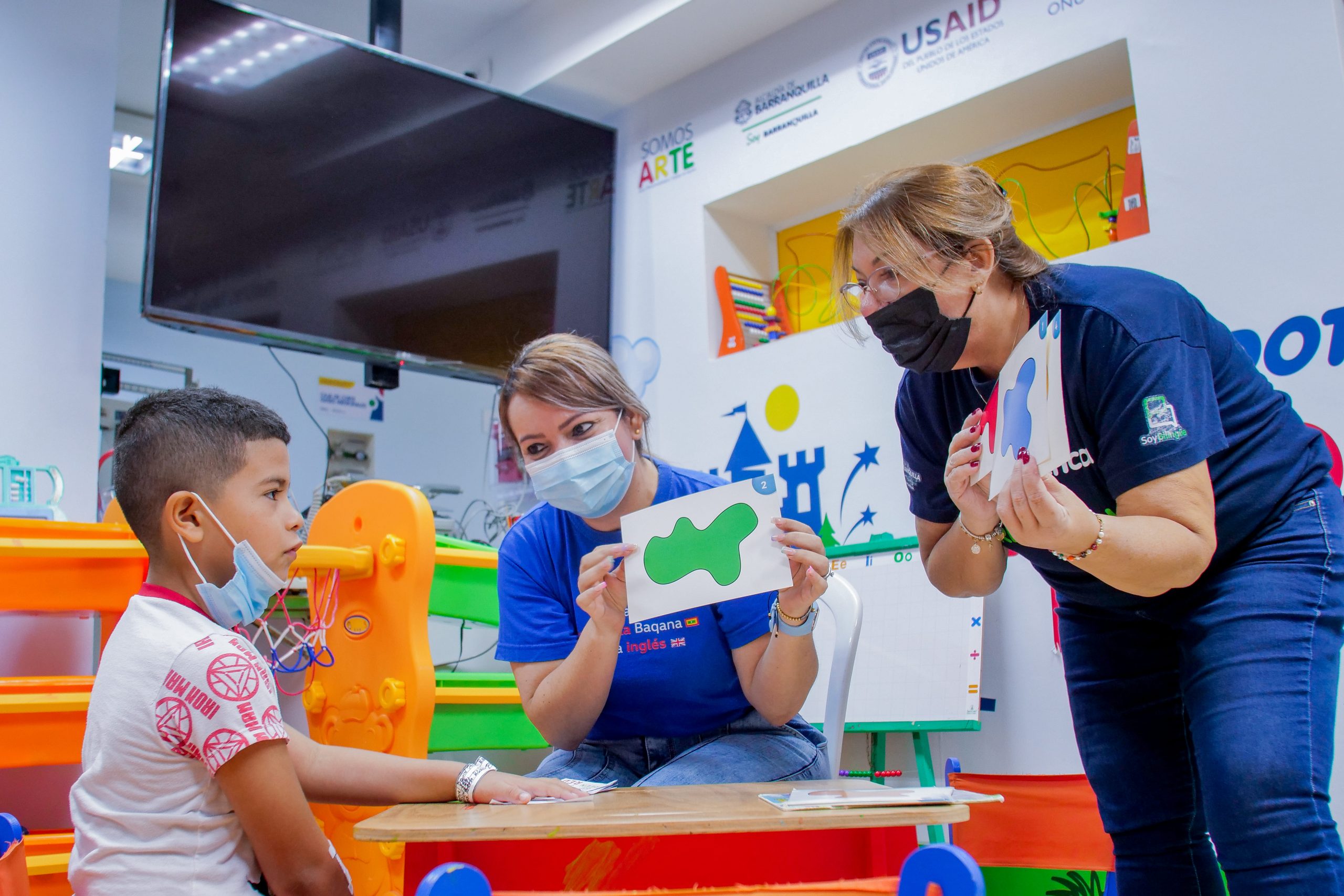 Niño en hospital recibiendo clases con carteleras por parte de dos profesoras