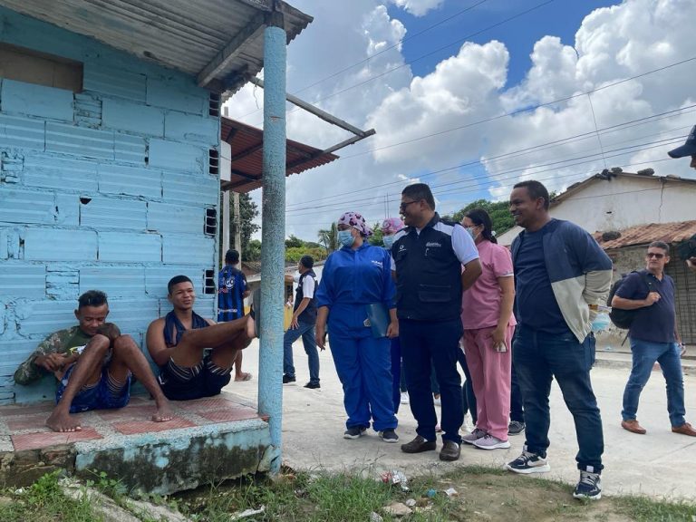 Funcionarios en calle charlando con dos habitantes sentados en una terraza