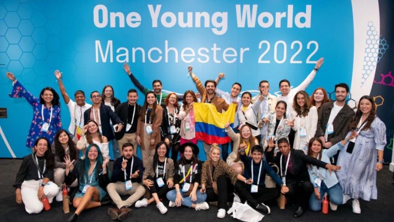 Grupo de jóvenes con bandera de Colombia con escarapelas y brazos arriba, de fondo anuncio sobre convocatoria 2022