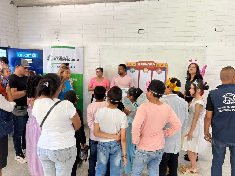 Niños con mascaras escuchando intervención alrededor de una funcionaria de educación