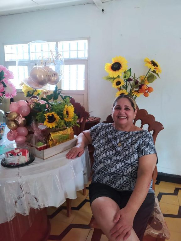 mujer sentada en mesa de comedor con arreglos de flores y feliz cumpleaños