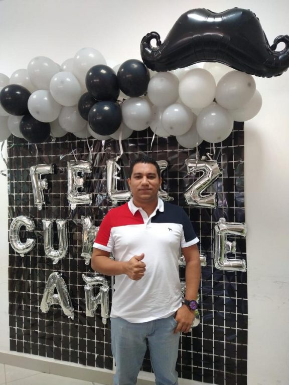 hombre de pie en pared decorada con globos blancos y negros y letras de feliz cumpleaños 