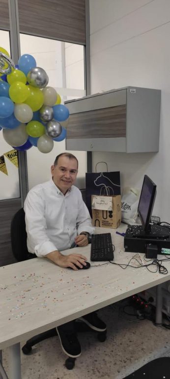 hombre sentado en su escritorio con confeti y decoración al fondo con globos verdes, azul, plateado y beiges