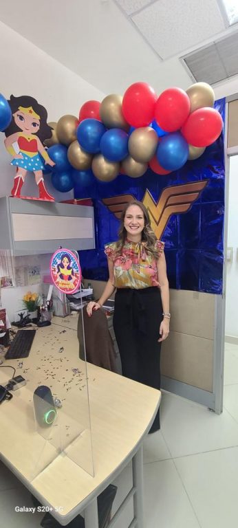 mujer de pie en su escritorio decorado con imágenes de la mujer maravilla y globos azules, rojos y dorados