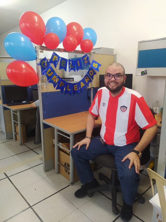 hombre con camisa de Junior sentado en su escritorio decorado con feliz cumpleaños