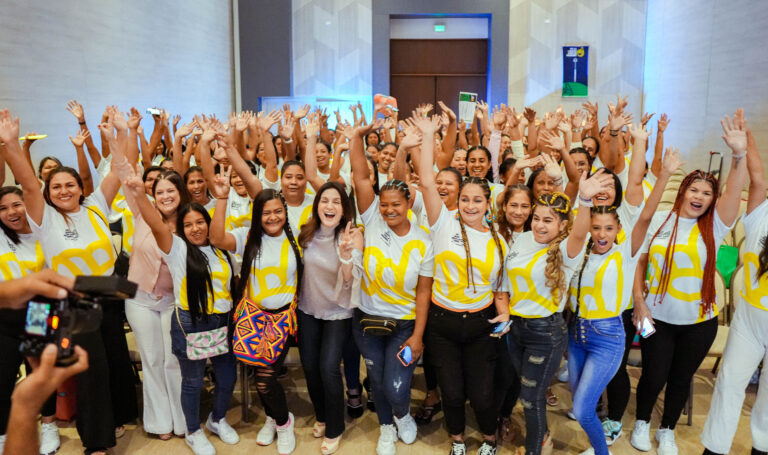 Grupo de beneficiarias con Katia Nule en evento, alzando las manos