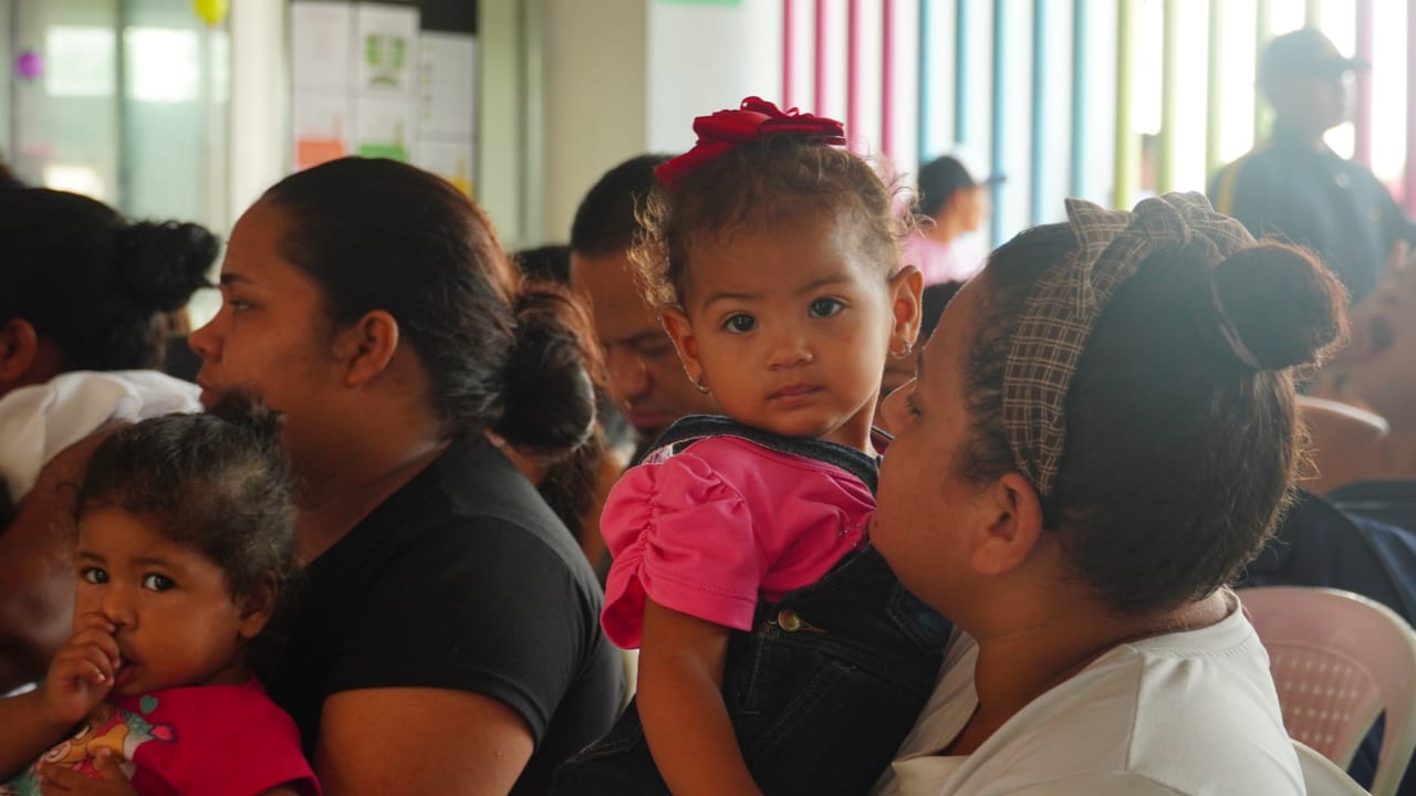 Grupo de personas y niñas sentadas durante la entrega de raciones alimentarias.