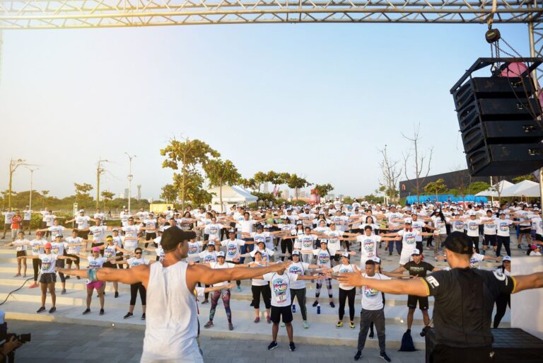 Grupo de personas frente escenario, participando en actividades de salud y deporte.