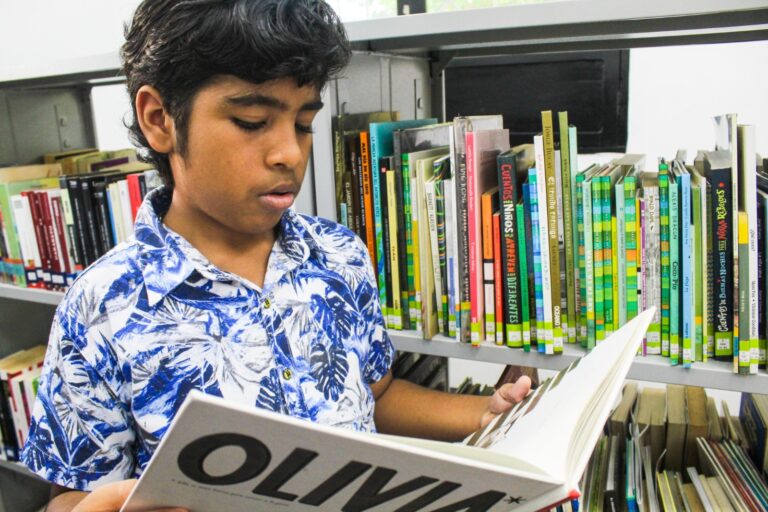 Un niño lee un libro en la biblioteca, rodeado de estanterías llenas.