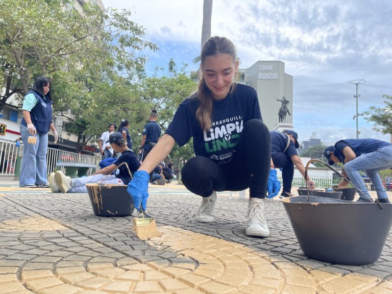 Voluntaria arrodillada pintando acera como parte del programa Barranquilla Limpia y Linda.