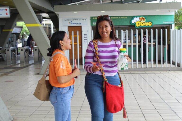 Funcionaria entregando volante de invitación a mujer en estación de TRansmetro