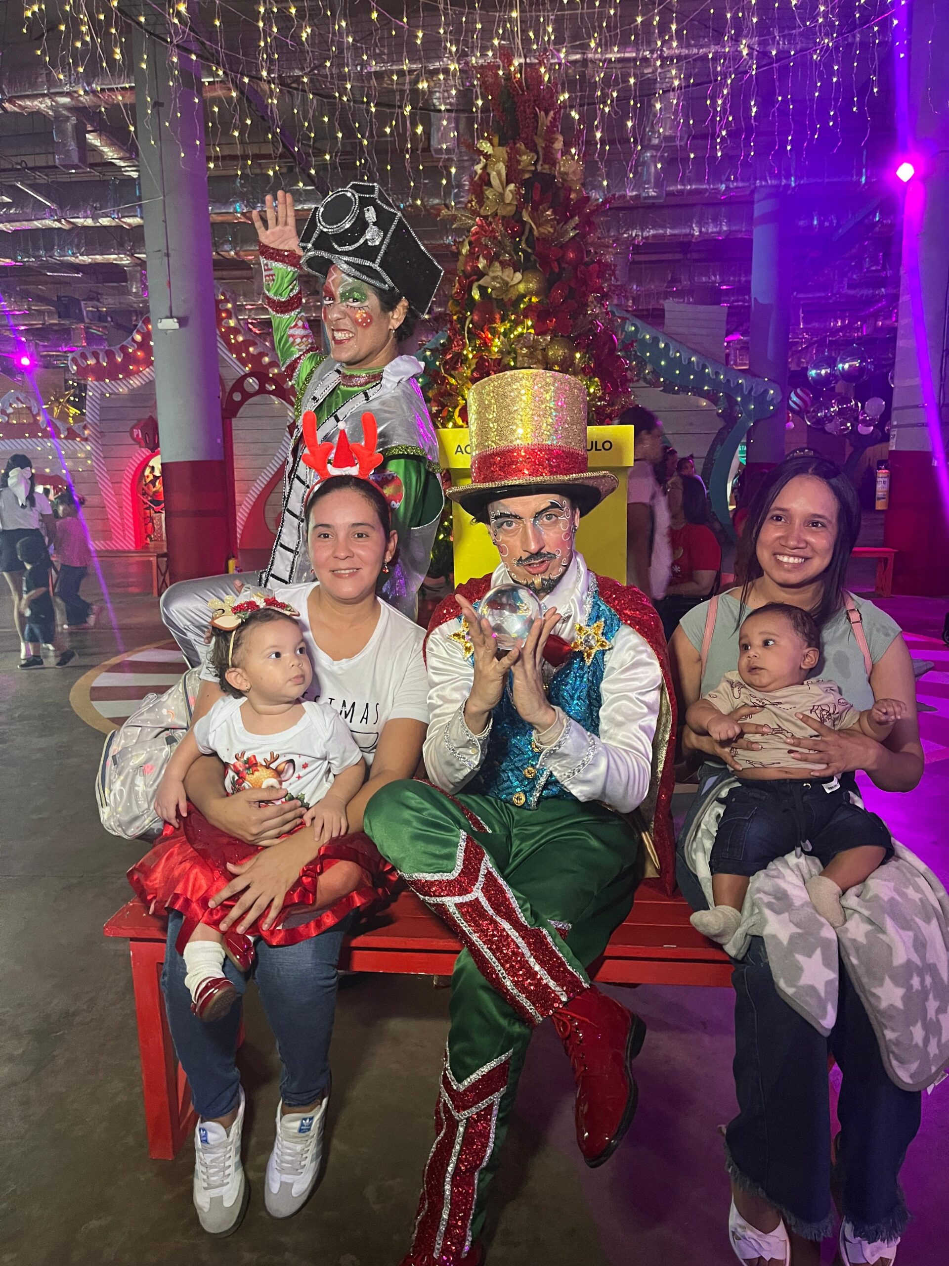 funcionarias sentadas con bebes en brazos, posan junto a personajes navideños.