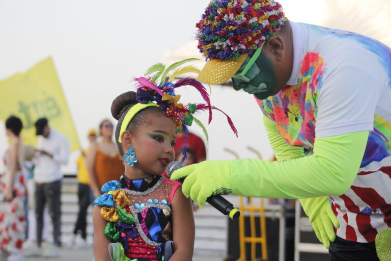 Niña hablando por un micrófono acompañada de un hacedor cultural en el Gran Malecón.