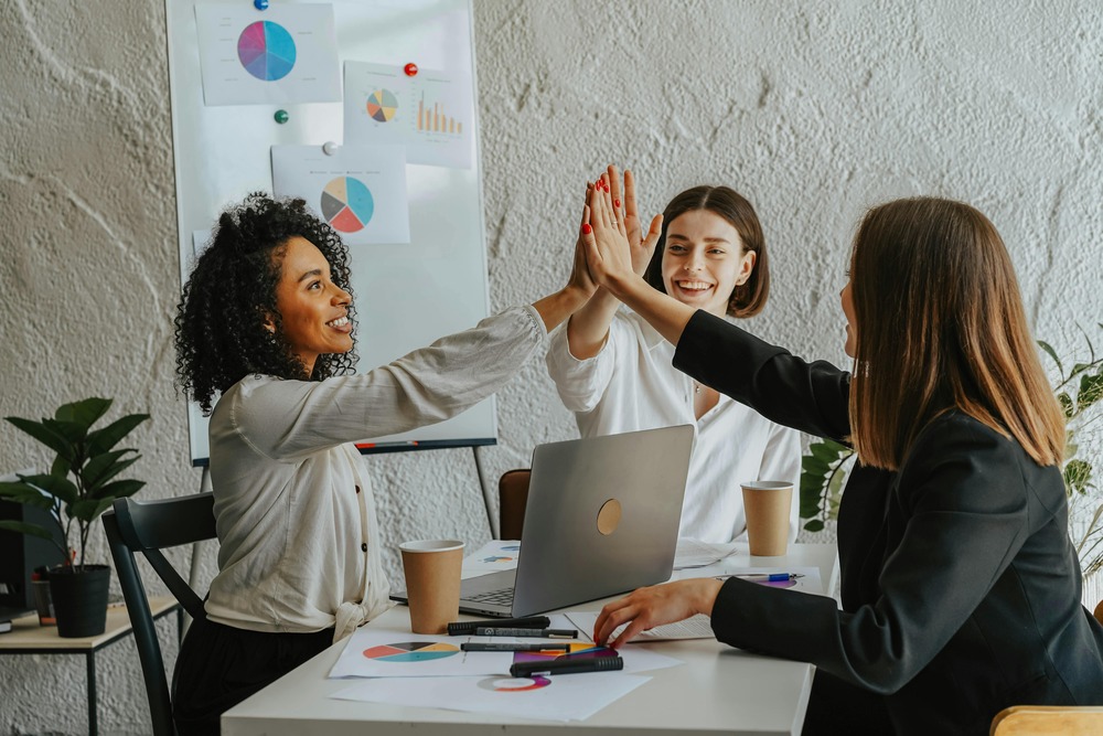 3 personas en una oficina, chocando las manos, representando trabajo en equipo