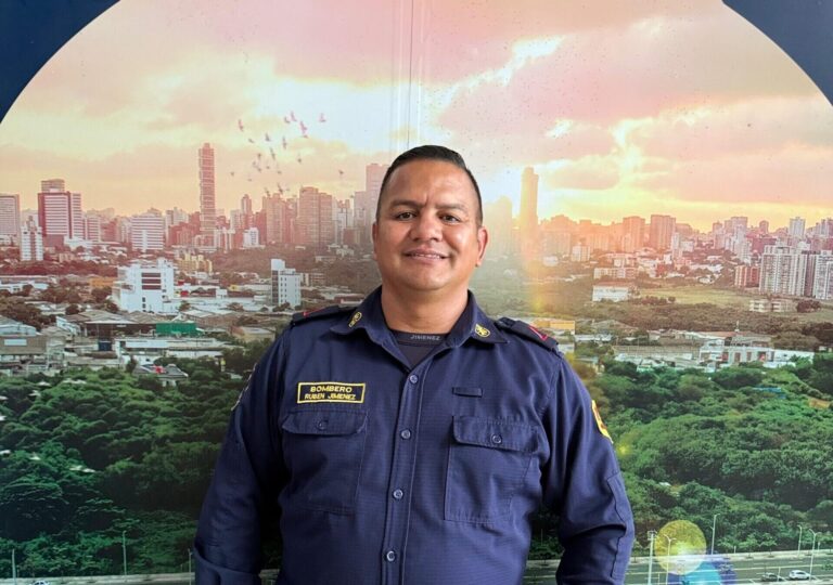 bombero Ruben Jimenez, posando con su uniforme oficial azul, junto al banner de una imagen de Barranquilla