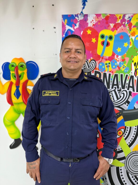 Ruben Jiménez Acuña, posando de pie con su uniforme azul, al lado de las decoraciones de Marimondas