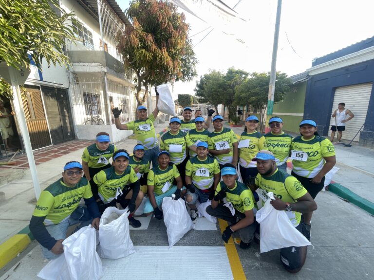 Grupo de voluntarios con camisetas verdes y gorras azules, reunidas en entorno a caminata ecológica CorrEco.