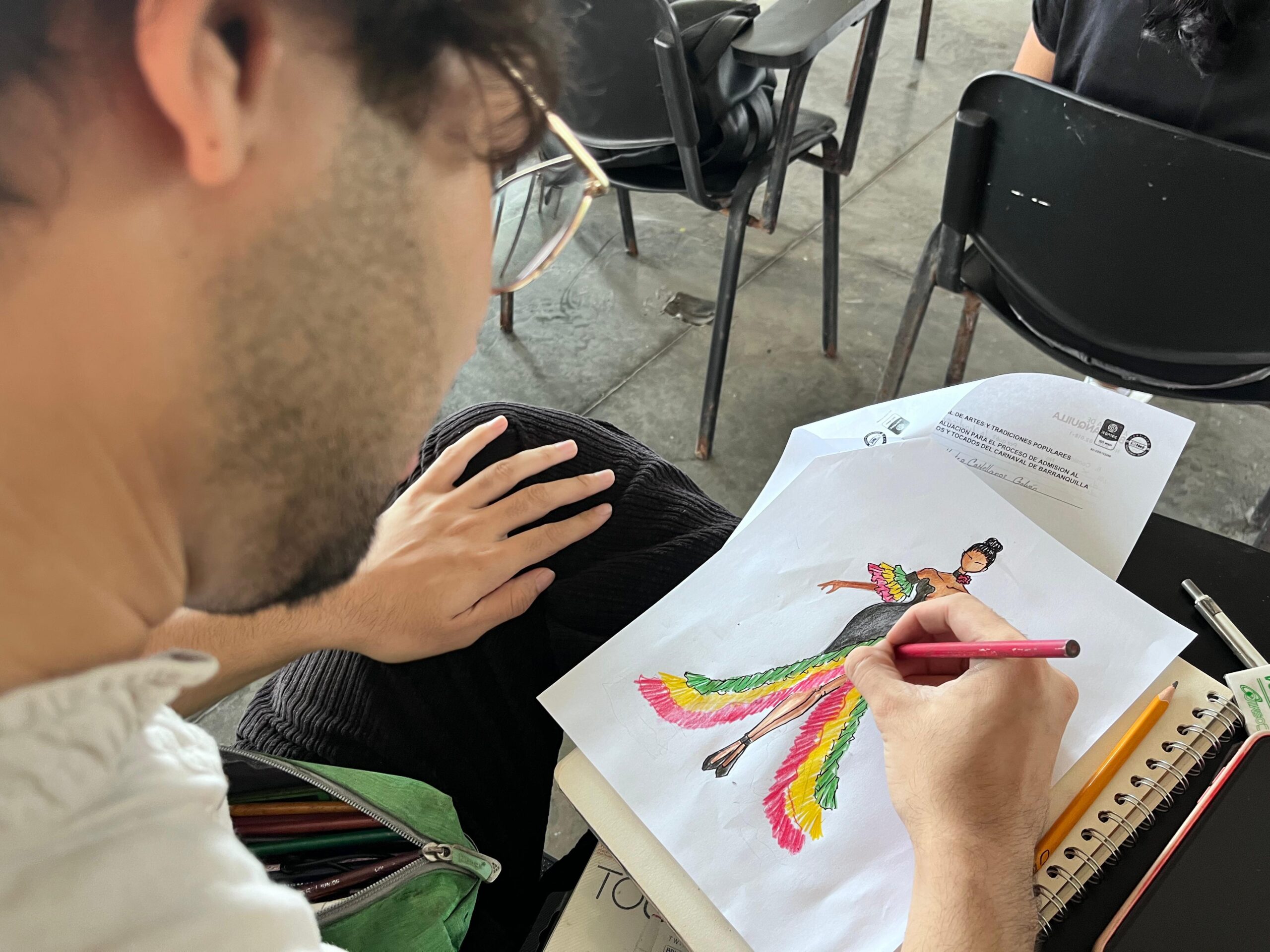 Estudiante de la Escuela Distrital de Arte colorea en papel un boceto de un vestido.