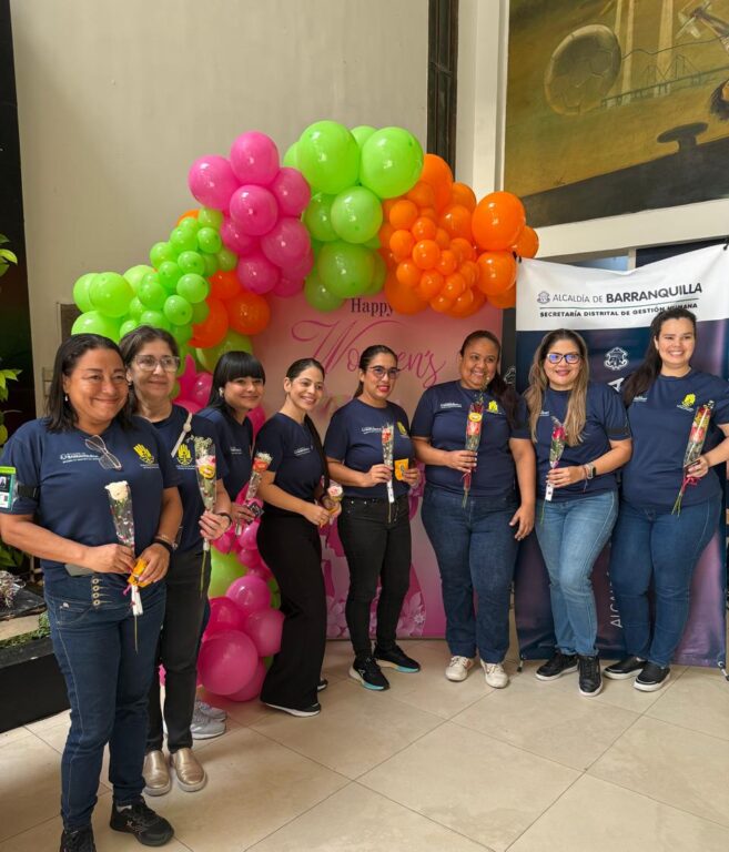 8 Funciojnarias con uniforme de Gestión del Riesgo, posan frente a decoración del Día de la Mujer