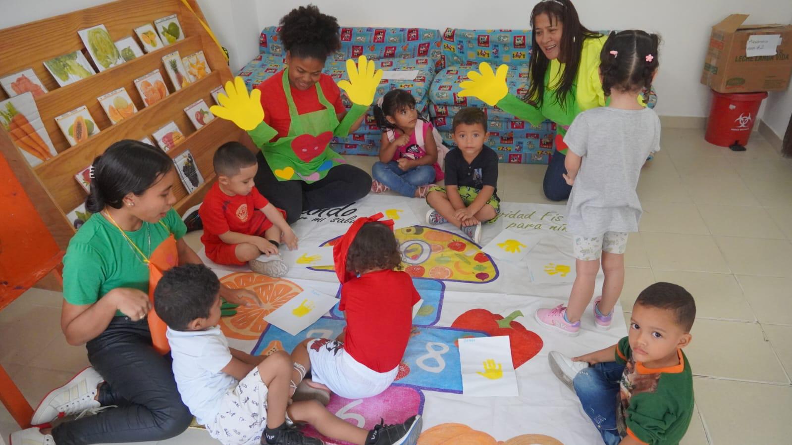 Niños y educadoras participan en una actividad lúdica con dibujos e ilustraciones de colores vivos.