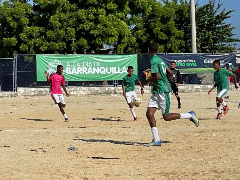 Grupo de jóvenes disputando un partido de fútbol en el marco de un torneo, en una cancha deportiva.