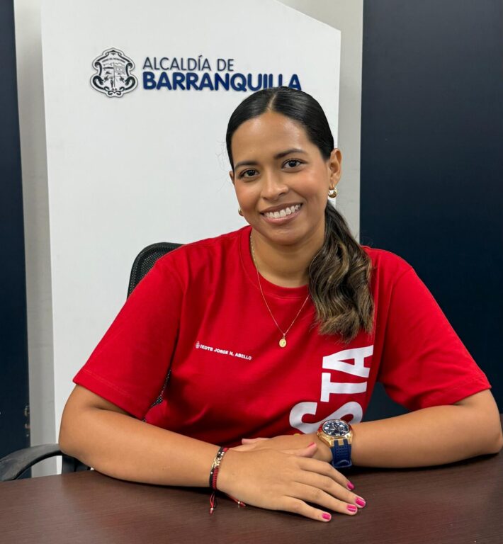 Funcionaria Betsy Caballero, con sueter rojo sentado frente a una mesa.