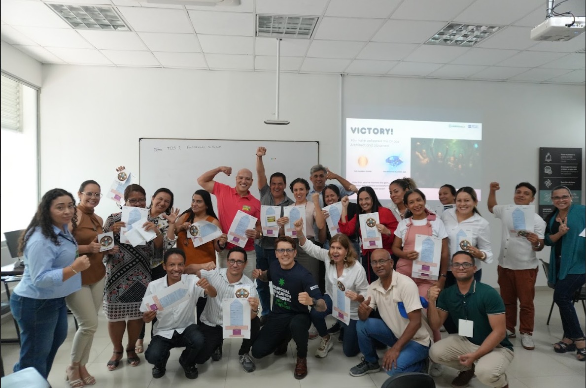 Grupo de docentes sonrientes en un aula, posando con certificados en la mano y mostrando gestos de celebración.