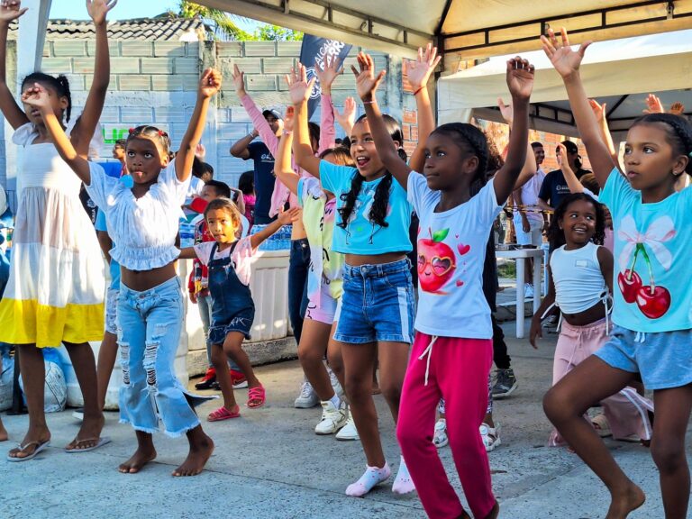 Niñas y niños participan con entusiasmo en una actividad de baile grupal al aire libre durante el programa "Diviértete en Familia".