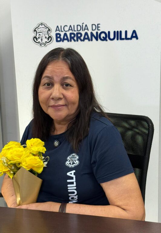 Funcionaria Leyla Cruz, sentada frente una mesa, sosteniendo en sus brazos flores amarillas.