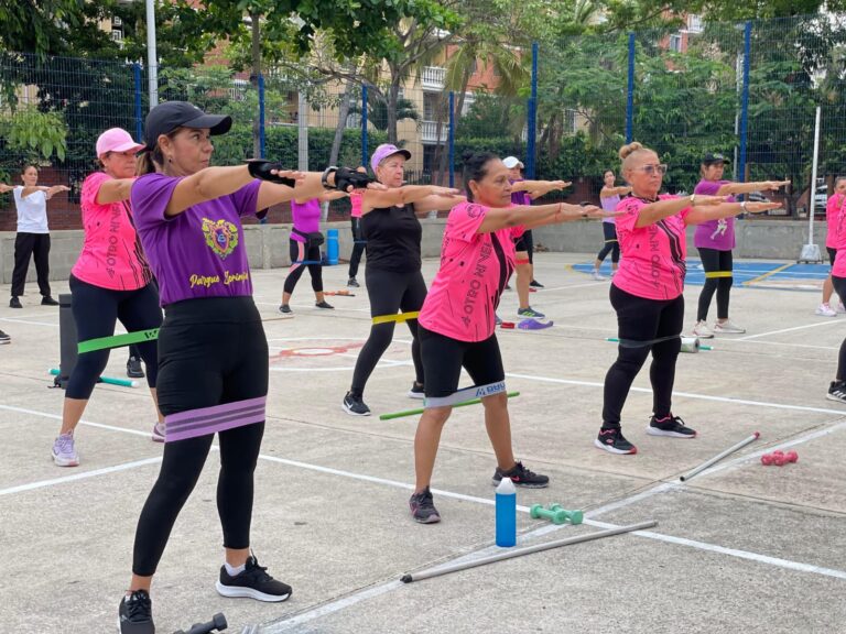 Mujeres realizan ejercicios grupales con bandas elásticas en programa deportivo "Muévete por Tres a Otro Nivel".