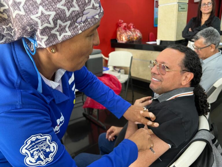 Ciudadano sonríe mientras recibe la vacuna contra la influenza por parte de una profesional de la salud.