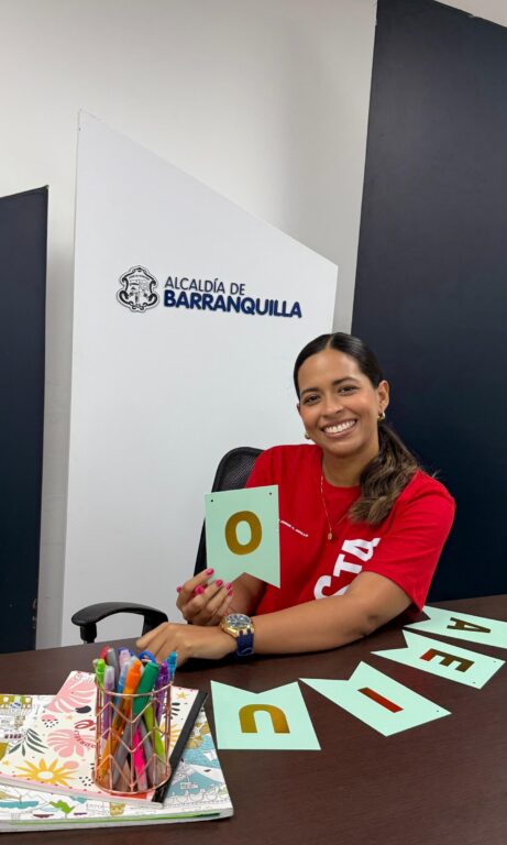 Funcionaria Betsy Caballero, sostiene una vocal en su mano, mientras esta rodeada de marcadores y letras