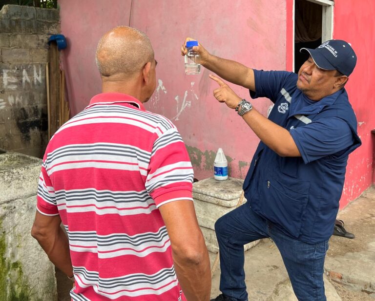 Funcionario de la Alcaldía muestra recipiente con agua y explica a ciudadano sobre posibles criaderos del mosquito del dengue.