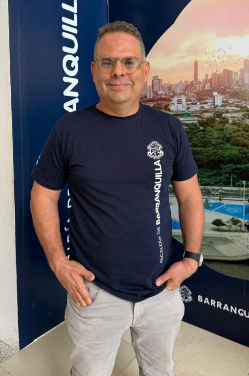 Funcionario Carlos Vergara, posa de pie en plano medio, con camiseta institucional y sus manos dentro de los bolsillos delanteros.