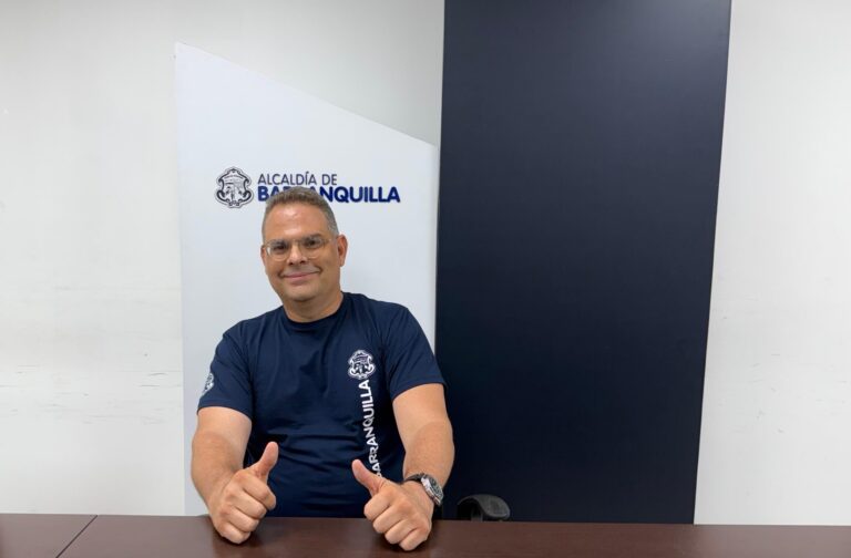 Funcionario Carlos Vergara, posa con uniforme institucional sentado frente a una mesa, con las manos con los dedos pulgares arriba, en señal de victoria.